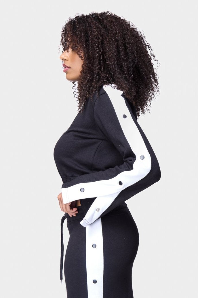 Black cropped track top with white snap buttons along the sleeves, creating a trendy and sporty look.